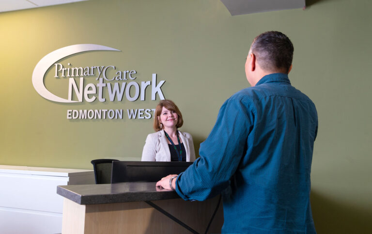 Two people standing at the Edmonton West Primary Care Network front reception area talking.